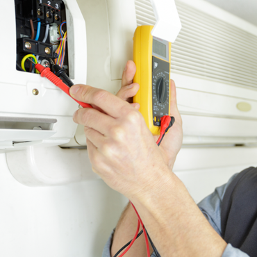 Technician using a multimeter to diagnose an air conditioning unit during maintenance service in Hidalgo County.