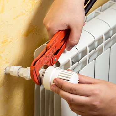 Hand using adjustable wrench to tighten a valve on a heating radiator, demonstrating HVAC maintenance and repair services.