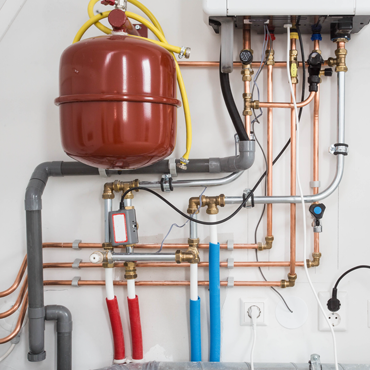 Heating system installation featuring copper and plastic piping, a red expansion tank, valves, and connections, illustrating HVAC infrastructure for efficient heating solutions in Hidalgo County.