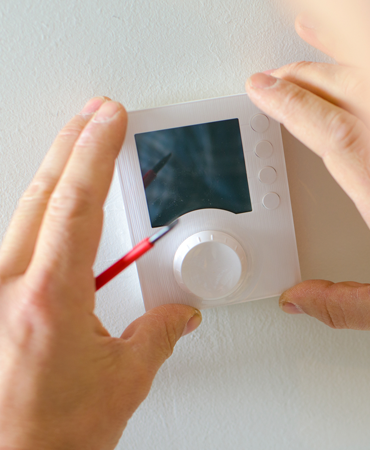 Hands adjusting a modern thermostat during installation, emphasizing home automation and energy efficiency.