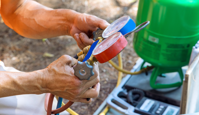 HVAC technician using pressure gauges on refrigerant lines for system diagnostics and repair services.