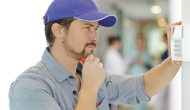 Man inspecting a thermostat with a screwdriver, illustrating HVAC repair services related to thermostat issues at L&S Air LLC.