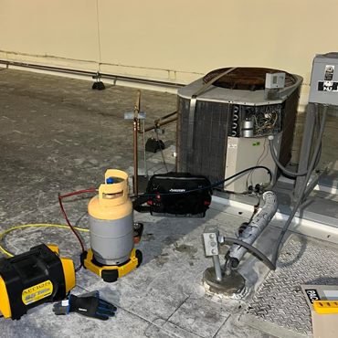 Ductless heating and cooling system installation with HVAC equipment, including a refrigerant tank and vacuum pump, on a concrete surface in a commercial setting.