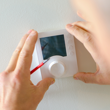 Hands installing a modern thermostat on a wall, emphasizing HVAC system upgrades and precise calibration for improved energy efficiency in the Rio Grande Valley.