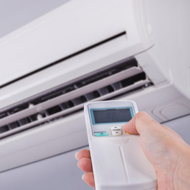 Hand holding remote control for a wall-mounted air conditioning unit, illustrating AC installation and operation in the Rio Grande Valley.
