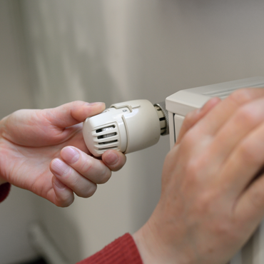 Person adjusting a heating system thermostat, demonstrating HVAC maintenance and comfort control in a home setting.